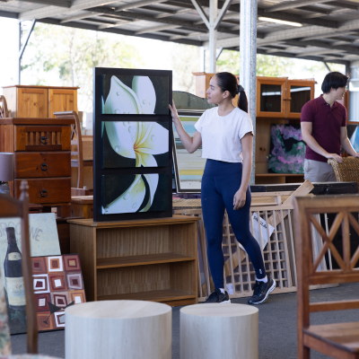 A lady walking through the recycling market looking at a painting with other furniture and fittings in the background.