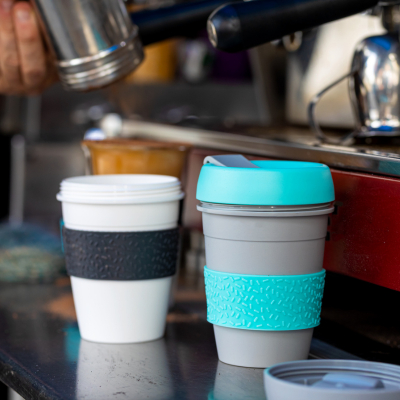 A blue and grey and white and black keep cup in front of a person making coffee