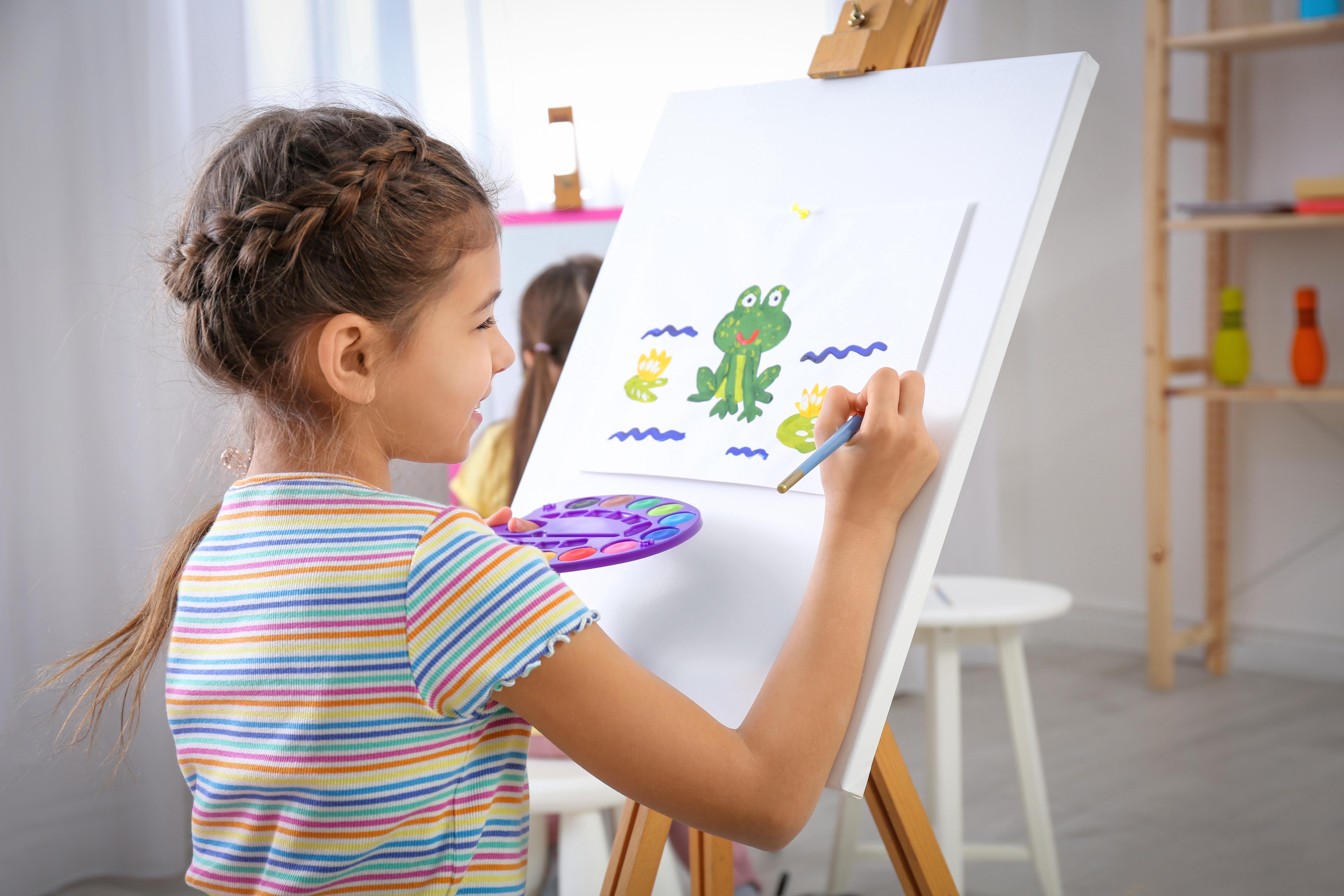 A girl painting a green frog on canvas