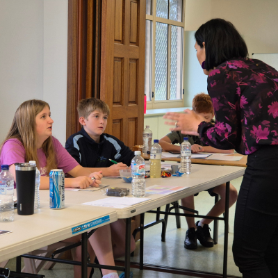 Two children sitting at a desk with a teacher instructing them