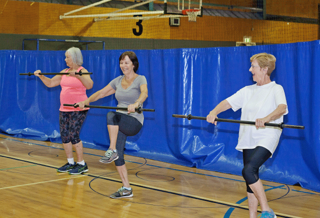 Three women holding exercise bars lifting their knees.