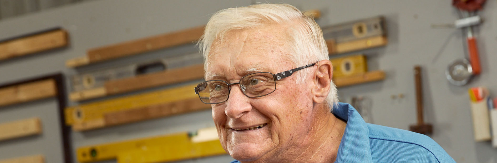 Elderly man wearing glasses and dressed in a blue polo shirt smiles