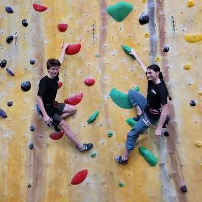 A boy and a girl smiling looking out as they climb the indoor rock wall
