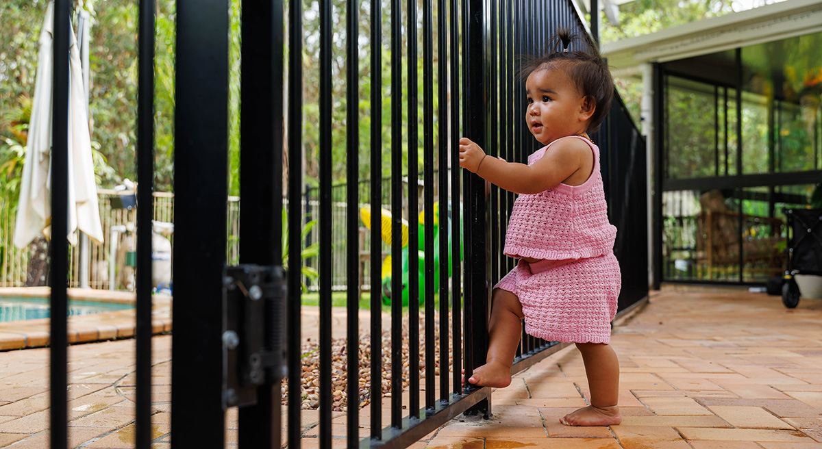 Young child stands on pool fence and stares at the pool