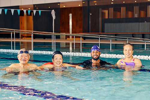 4 smiling adults swimming side by side in a pool