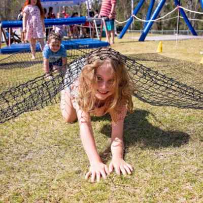 Young girl crawls through grass and under a net