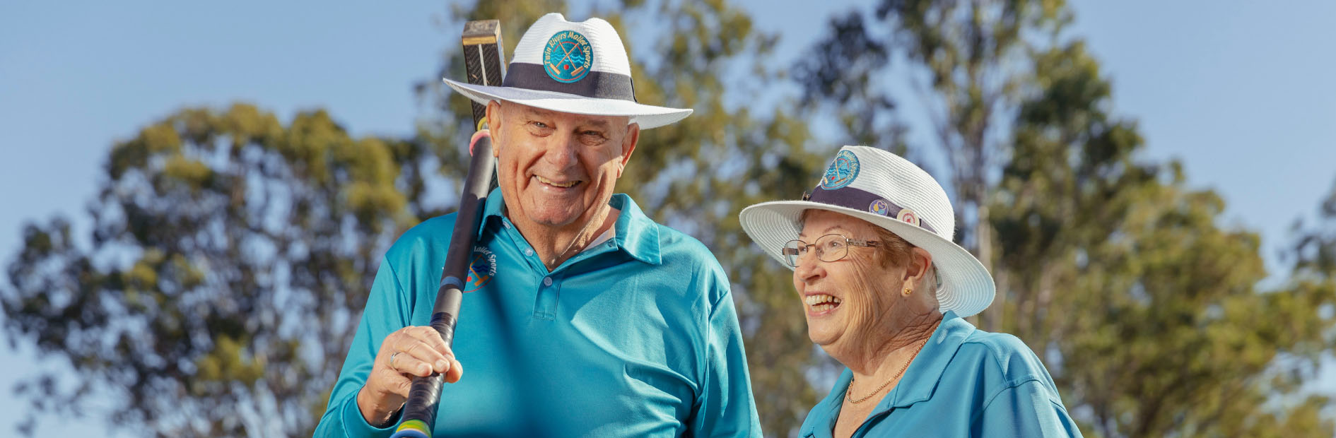 A elderly man and woman dressed in matching blue polo shirts carry gold clubs