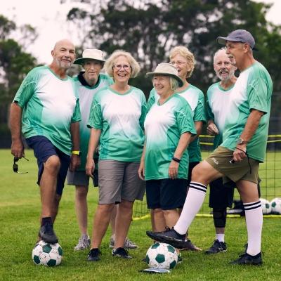 A group of people wearing green and white shirts kicking a football.