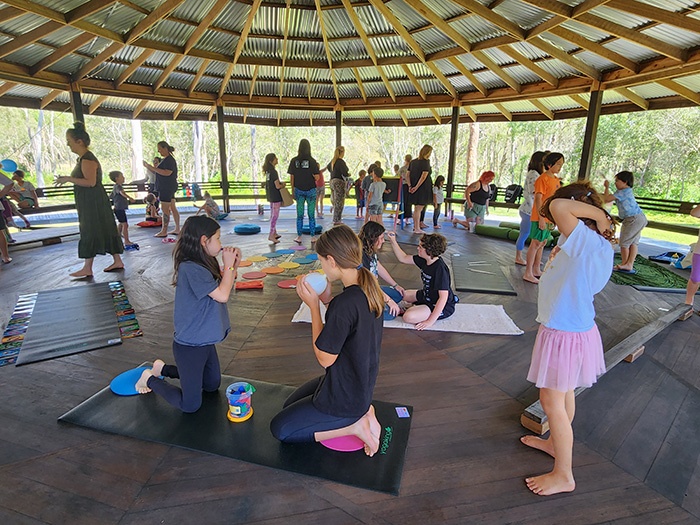 Children do activities while seated on yoga mats in outdoor undercover area