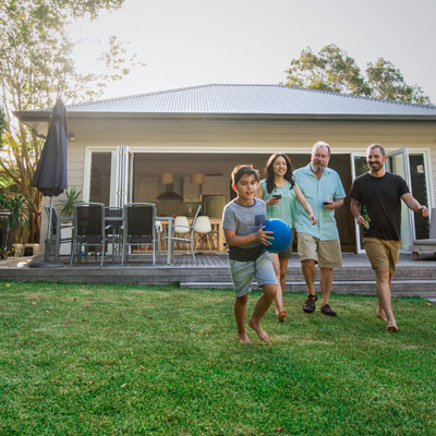 Adults holding drinks and laughing and young boy holding a ball and smiling in the back yard