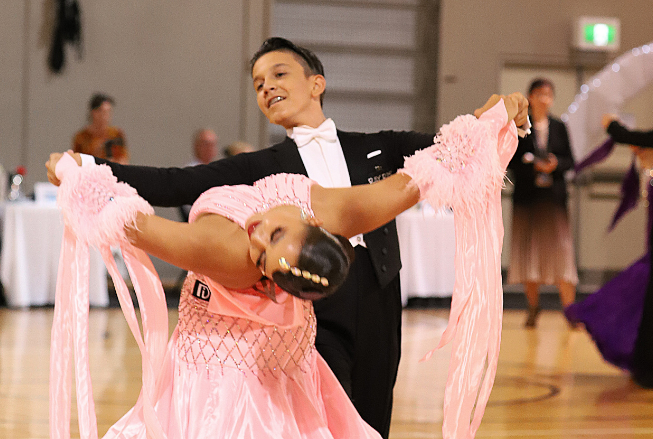 A man dressed in a suit and a lady dressed in a ball gown performing a ballroom dance.