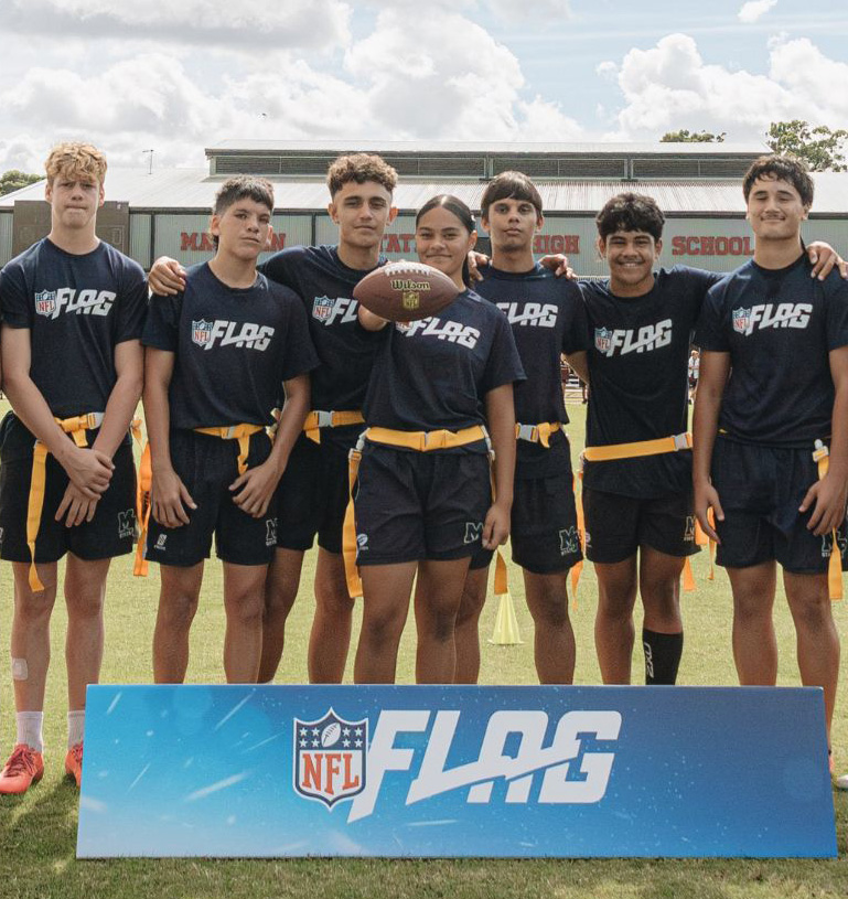 Group of male and female teenagers stand shoulder to shoulder wearing Flag tshirts. A girl in the centre of the group holds up a NFL ball.