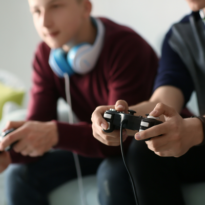 Two boys playing a game holding controllers and wearing headphones around their neck