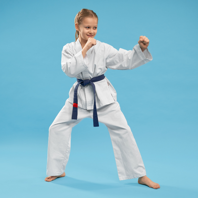 Girl dressed in white martial arts uniform poses with her fists up in a defensive pose