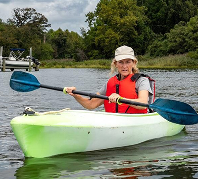 Woman wearing red lifejacket paddles kayak on river