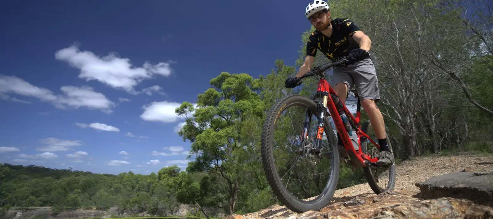 Man wearing a white helmet rides a red mountain bike down a rocky path