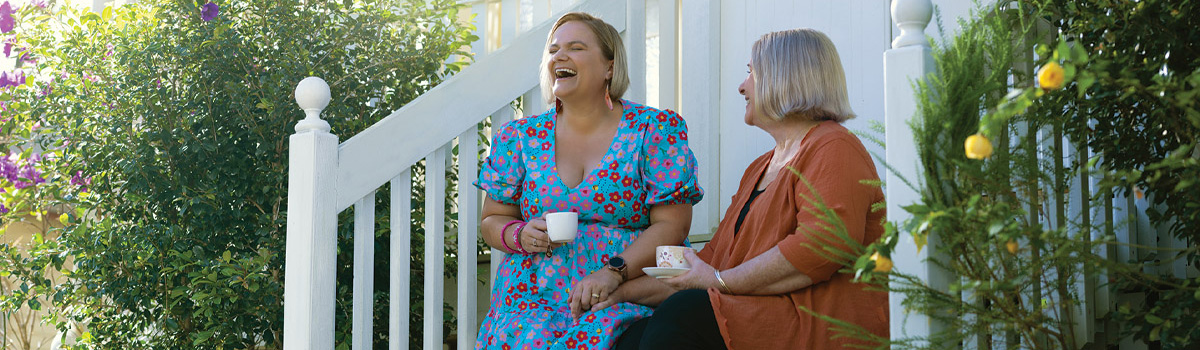 Two women sitting together on the front steps of a house laughing