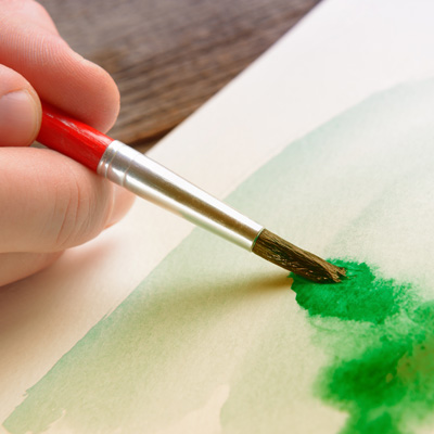 hand holding a brush with green water colour paint on it against a piece of paper